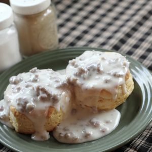 A plate of biscuits and gravy with a fork and salt and pepper shakers on the table