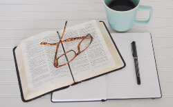 Open Bible with reading glasses, notebook, pen, and cup of coffee